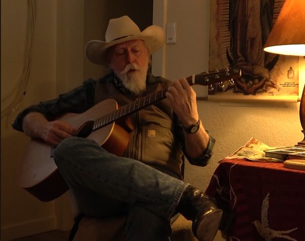 Musician in a cowboy hat playing acoustic guitar in a lamplit room