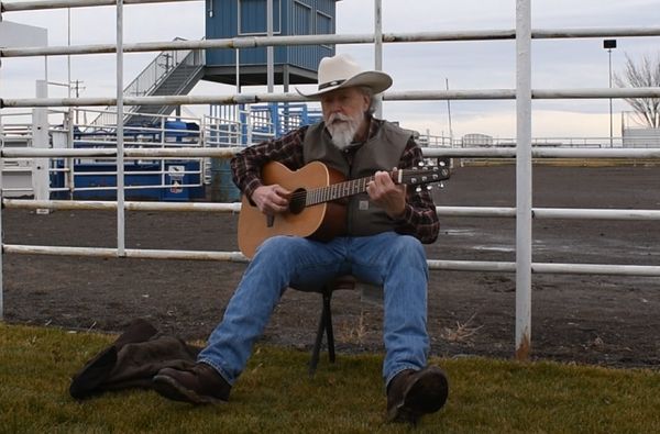Musician in a cowboy hat playing guitar on a stool outside an arena