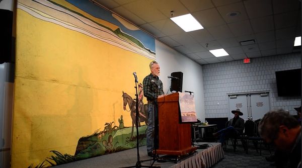 Performer at a podium on a stage in front of a Western mural