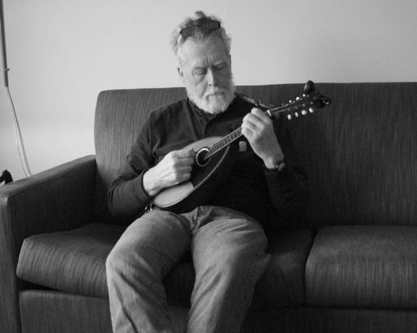 Black and white photo of a man playing mandolin on a sofa