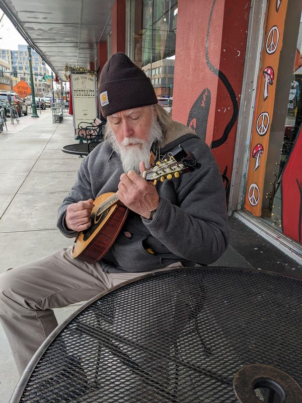 Musician in a knit cap playing mandolin at a sidewalk table