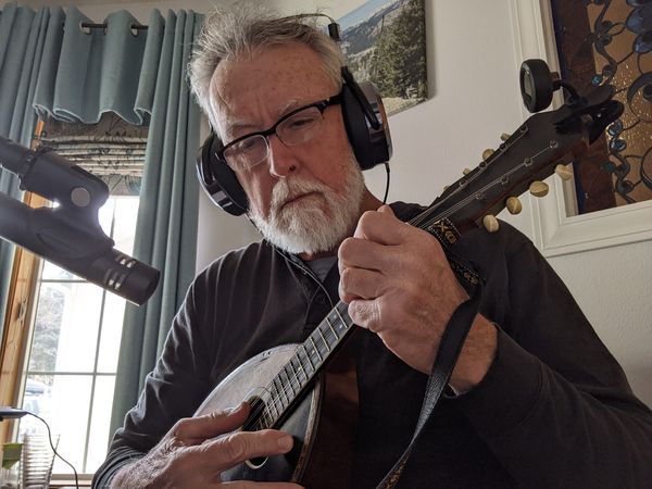 Musician wearing headphones recording a mandolin part at a microphone